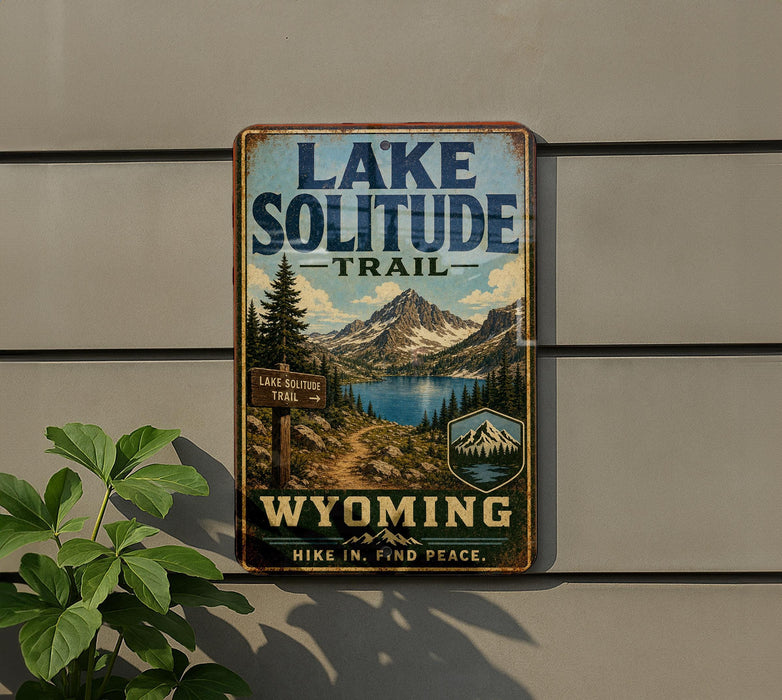 A vintage-style metal sign for the Lake Solitude Trail in Wyoming, featuring a scenic mountain landscape and a trail sign.