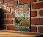 A vintage-style sign for Lancaster County, Pennsylvania, featuring an illustration of a farm and a horse-drawn carriage, mounted on a brick wall.