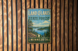 A vintage metal sign for the Land O'Lakes State Forest in Minnesota, featuring a scenic landscape with pine trees, a lake, and mountains.