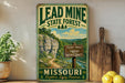 A vintage-style metal sign for the Lead Mine State Forest in Missouri, featuring a scenic mountain landscape and trail signs.
