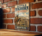 A vintage metal sign for the Little Big Horn Battlefield National Monument in Montana, featuring an illustration of a Native American on horseback.