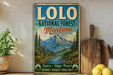 A vintage-style metal sign for Lolo National Forest, Montana, featuring a scenic mountain landscape with pine trees and a river.