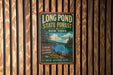 A vintage-style metal sign for Long Pond State Forest in New York, featuring a scenic image of a lake, forest, and canoe.
