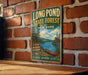 A vintage-style metal sign for Long Pond State Forest in New York, featuring a scenic illustration of a lake, forest, and canoe.