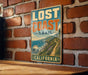 A vintage-style metal sign with the text "LOST COAST TRAIL" and "CALIFORNIA" is displayed on a brick wall.