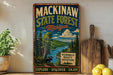 A vintage-style metal sign for Mackinaw State Forest in Michigan, featuring a scenic illustration of a forest, a moose, and a river.