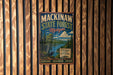A vintage metal sign for Mackinaw State Forest in Michigan, featuring a scenic illustration of a forest landscape with a moose and a river.