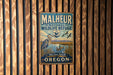 A metal sign with the text "MALHEUR NATIONAL WILDLIFE REFUGE" and an illustration of birds in a natural setting, mounted on a wooden wall.