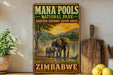 A vintage-style sign for the Mana Pools National Park in Zimbabwe, featuring an illustration of an elephant and a sunset over a body of water.