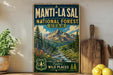 A vintage-style sign for the Manti-La Sal National Forest in Utah, featuring a scenic mountain landscape with pine trees, wildflowers, and a stream.