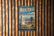 A vintage metal sign for the National Historic Site in Manzanar, California, featuring a mountain landscape and a lookout tower.