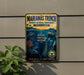 a metal sign with a marine theme, hanging on a wall next to a plant.