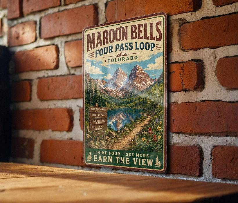 A vintage-style metal sign advertising the Maroon Bells Four Pass Loop in Colorado, featuring a scenic mountain landscape with a lake and trail.