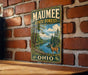 A vintage metal sign for the Maumee State Forest in Ohio, featuring a scenic illustration of a deer in the foreground with a river and forest in the background.