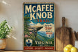 A vintage-style metal sign for the Mcafee Knob Trail in Virginia, featuring a scenic mountain landscape and encouraging visitors to "Take in the View! Keep it Wild!" The sign is displayed on a wooden shelf, with a potted plant and a wooden cutting board nearby.