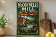 A vintage-style metal sign for McConnells Mill State Park in Pennsylvania, featuring a scenic illustration of a mill and a waterfall.
