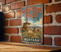 A vintage-style metal sign for Medicine Rocks State Park in Montana, featuring a scenic landscape with rock formations and mountains.