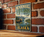A vintage metal sign for Mendenhall Wetlands State Game Refuge in Alaska, featuring a moose and a bird in a scenic landscape.