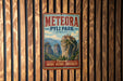 A vintage-style metal sign for Meteora Pyli Park in Greece, featuring a mountain landscape with a castle-like structure on top.