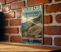 A vintage-style metal sign for Miguasha National Park, Canada, featuring a scenic coastal landscape with mountains, trees, and a rocky shoreline.