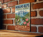 A vintage-style metal sign with a mountain landscape and a bird, mounted on a brick wall.