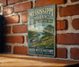 A vintage-style metal sign for the Mississippi Hills National Heritage Area, featuring a scenic illustration of a river and surrounding landscape.