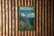 A vintage metal sign for Modoc National Forest, California, featuring a scenic landscape with mountains, forests, and a lake.