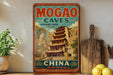 A vintage-style sign advertising the Mogao Caves in China, featuring a colorful illustration of a temple and a Buddhist figure.