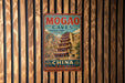 A vintage-style metal sign with the text "MOGAO CAVES DUNHANG-GONGU CHINA" and an illustration of a pagoda, hanging on a wooden wall.