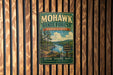 A vintage metal sign for Mohawk State Forest in Connecticut, featuring a scenic landscape with pine trees, a lake, and mountains.