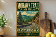 A vintage-style metal sign for the Mohawk Trail State Forest in Massachusetts, featuring a scenic mountain landscape with a winding road.
