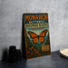 A vintage-style metal sign with the text "MONARCH BUTTERFLY BIOSPHERE RESERVE MEXICO" and an illustration of a butterfly. The sign is placed on a gray countertop next to a stack of black camera lenses.