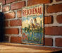 A vintage metal sign on a brick wall, featuring an illustration of a castle and a lake, with the text "MONASTIC ISLAND OF REICHENAU GERMANY" and "A UNESCO WORLD HERITAGE SITE".