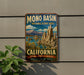 A vintage-style metal sign for the Mono Basin National Scenic Area in California, featuring a scenic landscape with mountains, water, and unique rock formations.
