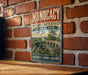 A vintage metal sign with the text "MONOCACY NATIONAL BATTLEFIELD MARYLAND" and an illustration of a cannon on a bridge, mounted on a brick wall.