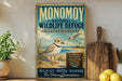 A vintage-style metal sign for the Monomoy National Wildlife Refuge in Massachusetts, featuring an illustration of a bird on a beach and text promoting the refuge's mission to protect wildlife, preserve natural heritage, and provide a wildlife-water-wonder for future generations.