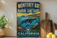 A vintage-style metal sign for Monterey Bay National Marine Sanctuary, featuring an illustration of marine life and the text "California" and "Explore, Protect, Inspire".