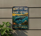 A vintage-style metal sign for Monterey Bay National Marine Sanctuary, featuring an illustration of marine life and the text "California" and "Explore, Protect, Inspire".