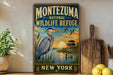 A vintage-style metal sign for the Montezuma National Wildlife Refuge in New York, featuring an illustration of a heron and ducks in a lake at sunset.