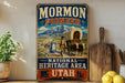 A vintage-style metal sign for the Mormon Pioneer National Heritage Area in Utah, featuring an illustration of a covered wagon and people traveling through a scenic landscape.