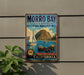 A vintage-style metal sign for Morro Bay State Marine Recreational Management Area, featuring a sailboat and sea otters, is displayed on a wall next to a plant.