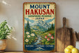 A vintage-style sign for Mount Hakusan, a biosphere reserve in Japan, featuring a mountain landscape with flowers and a stream.