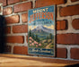 A vintage-style metal sign for Mount Jefferson State Natural Area in North Carolina, featuring a mountain landscape with pine trees and pink flowers.