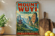 a vintage-style sign for Mount Wuyi, China, with a mountainous landscape and traditional Chinese architecture. The sign is displayed on a shelf, surrounded by various items such as a potted plant, a wooden cutting board, and some lemons.