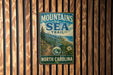 A vintage metal sign with the text "MOUNTAINS TO SEA TRAIL NORTH CAROLINA" is displayed on a wooden wall.