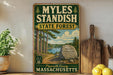 A vintage-style sign for Myles Standish State Forest in Plymouth County, Massachusetts, featuring a scenic illustration of a forest and a lake.