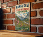 A vintage-style metal sign with the text "NANDA DEVI AND VALLEY OF FLOWERS NATIONAL PARKS INDIA" and "UTTARAKHAND, INDIA" is displayed on a brick wall.