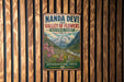 A vintage-style metal sign with the text "Nanda Devi and Valley of Flowers National Parks, India" is displayed on a wooden wall.