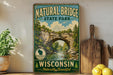A vintage-style sign for Natural Bridge State Park in Wisconsin, featuring a scenic image of the bridge surrounded by trees and water.