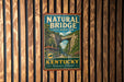 A vintage-style metal sign for Natural Bridge State Resort Park in Kentucky, featuring a scenic image of the bridge surrounded by lush greenery.